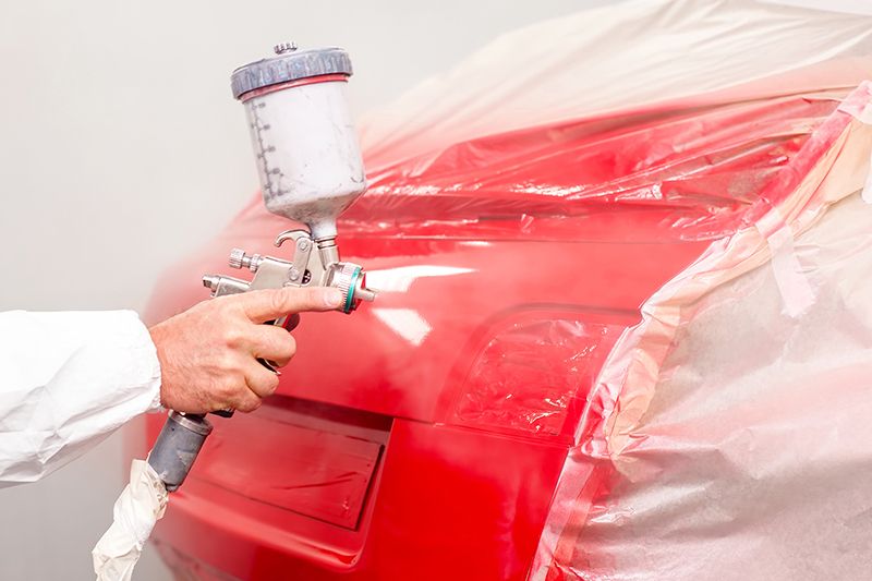 Eine Person verwendet eine Sprühpistole, um ein rotes Auto zu lackieren