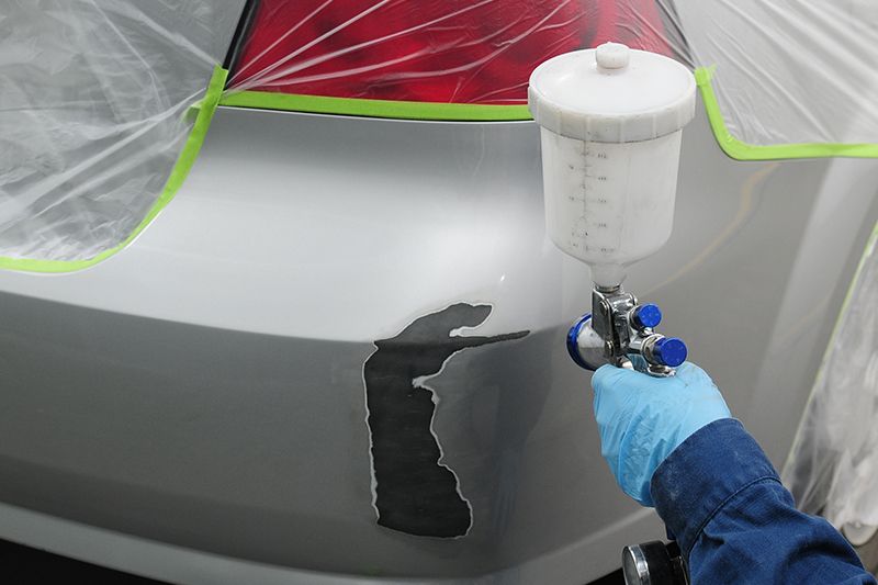 Eine Person lackiert ein Auto mit einer Sprühpistole in einer Werkstatt